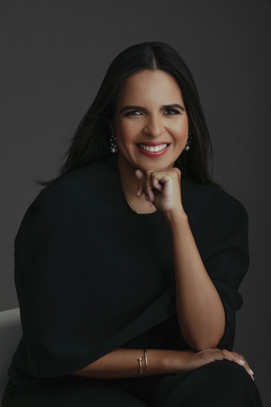 Retrato de Janis Santaella sonriente, vestida de negro sobre un fondo oscuro